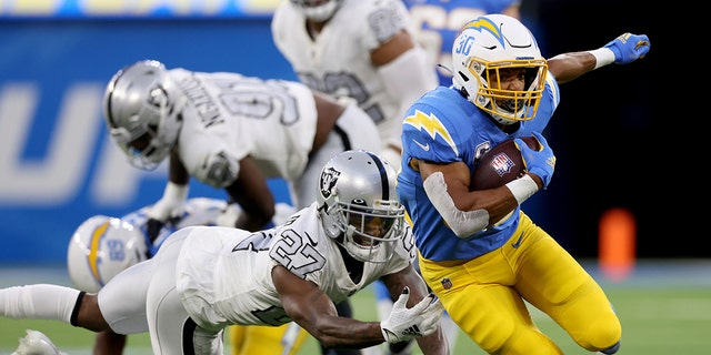 Austin Ekeler #30 of the Los Angeles Chargers cuts back to avoid the tackle of Trayvon Mullen Jr. #27 of the Las Vegas Raiders during a 28-14 win over the Las Vegas Raiders at SoFi Stadium on October 04, 2021 in Inglewood, California.