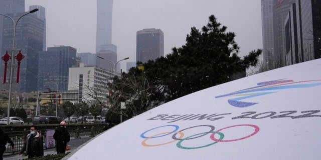 Obyvatelia prechádzajú okolo loga zimných olympijských hier v Pekingu neďaleko centrálnej obchodnej štvrte v čínskom Pekingu v piatok, január.  21, 2022. Čína obmedzuje štafetu s pochodňou pre zimné olympijské hry len na tri dni kvôli obavám z koronavírusu, uviedli v piatok organizátori.  (AP Photo/Ng Han Guan)