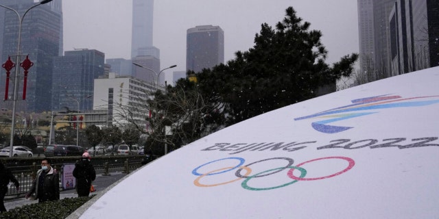 Residents walk past the Winter Olympics logo near the central business district in Beijing, China, Friday, Jan. 21, 2022. (AP)