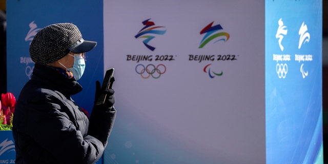 Seorang wanita mengenakan masker wajah untuk melindungi diri dari COVID-19 duduk di dekat lanskap yang dihiasi dengan logo Olimpiade dan Paralimpiade Musim Dingin Beijing di jalan perbelanjaan pejalan kaki di Beijing, Sabtu, 29 Januari 2020.  15, 2022.