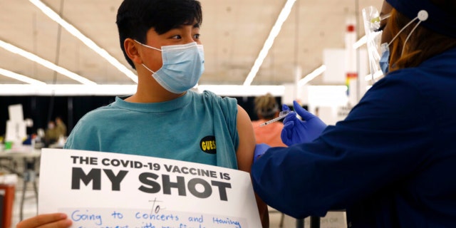 Lucas Kittikamron-Mora, 13, holds a sign in support of COVID-19 vaccinations as he receives his first Pfizer vaccination at the Cook County Public Health Department, May 13, 2021 in Des Plaines, Ill.