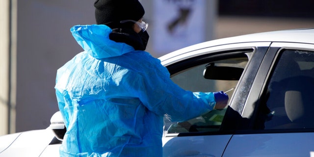 A medical technician performs a nasal swab test on a motorist queued up in a line at a COVID-19 testing site near All City Stadium Thursday, Dec. 30, 2021, in southeast Denver.  (AP Photo/David Zalubowski)