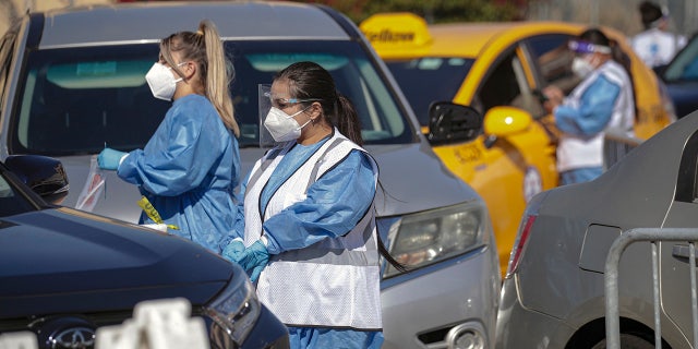 Healthcare worker go car to car at a drive-through COVID19 testing facility established by Total Testing Solutions in Boyle Heights on Tuesday, Jan. 25, 2022 in Los Angeles. (Irfan Khan / Los Angeles Times via Getty Images)