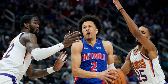 Detroit Pistons guard Cade Cunningham (2) drives to the basket as Phoenix Suns center Deandre Ayton, left, and forward Mikal Bridges (25) defend during the first half of an NBA basketball game, Sunday, Jan. 16, 2022, in Detroit.