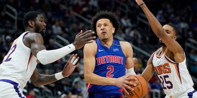 Detroit Pistons guard Cade Cunningham (2) drives to the basket as Phoenix Suns center Deandre Ayton, left, and forward Mikal Bridges (25) defend during the first half of an NBA basketball game, Sunday, Jan. 16, 2022, in Detroit.