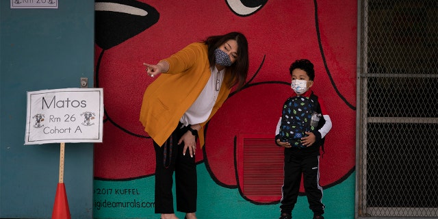 Kindergarten teacher Lilia Matos and student Jesus Mendes stand outside a classroom on April 13, 2021, during the first day of in-person learning at Heliotrope Avenue Elementary School in Maywood, California.  