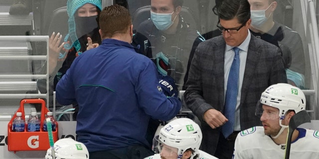Seattle Kraken fan Nadia Popovici, upper left, gestures toward Vancouver Canucks assistant equipment manager Brian "Red" Hamilton, second from left, after they were introduced during the first period of an NHL hockey game, Saturday, Jan. 1, 2022, in Seattle.