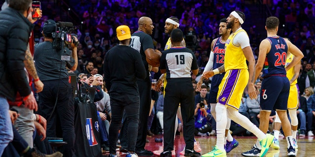 Los Angeles Lakers' Carmelo Anthony, top center, is held back by officials after having a word with a fan in the stands during the second half of an NBA basketball game against the Philadelphia 76ers, 星期四, 一月. 27, 2022, 在费城.
