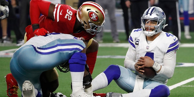 Dallas Cowboys quarterback Dak Prescott, right, holds the ball after recovering his own fumble on a sack by San Francisco 49ers defensive end Charles Omenihu (92) during the second half of an NFL wild-card playoff football game in Arlington, Texas, Sunday, Jan. 16, 2022.