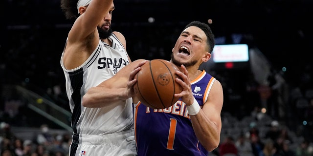 Phoenix Suns guard Devin Booker (1) is fouled as he drives to the basket against San Antonio Spurs guard Derrick White, 剩下, during the second half of an NBA basketball game, 星期一, 一月. 17, 2022, in San Antonio.