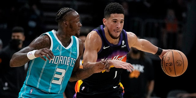 Phoenix Suns guard Devin Booker drives to the basket past Charlotte Hornets guard Terry Rozier during the first half of an NBA basketball game on Sunday, Jan. 2, 2022, a Charlotte, N.C.
