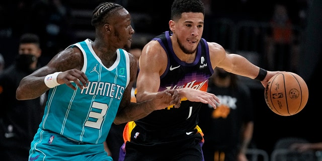 Phoenix Suns guard Devin Booker drives to the basket past Charlotte Hornets guard Terry Rozier during the first half of an NBA basketball game on Sunday, Jan. 2, 2022, in Charlotte, N.C.