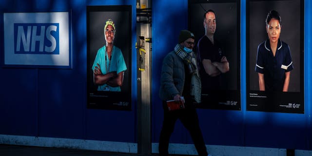 A pedestrian walks past portraits of National Health Service (NHS) employees on palisades outside a temporary structure on Friday, January 7, 2022 (Chris J. Ratcliffe / Bloomberg via Getty Images)