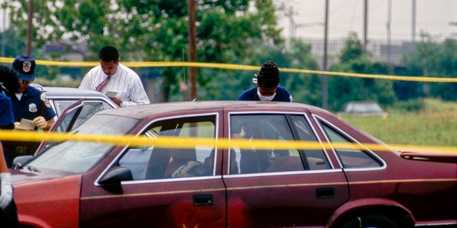 DC homicide detectives examine evidence in a car at a murder crime scene, Washington DC, 1996. The victim's body was found in the parked car.