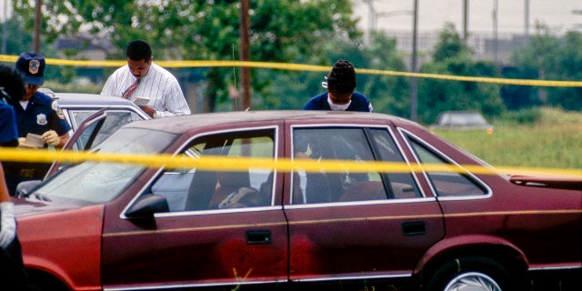 DC homicide detectives examine evidence in a car at a murder crime scene, Washington DC, 1996. The victim's body was found in the parked car.