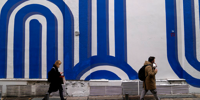 Pedestrians wearing face masks to curb the spread of coronavirus pass in front of the mural "Waves" by the artist Adioshpe in Athens, Griekeland, Woensdag, Jan.. 12, 2022.