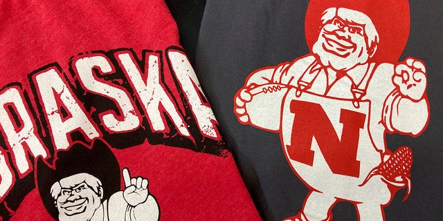 Nebraska Huskers t-shirts featuring new cartoon mascot Herbie Husker, left, and old cartoon mascot, right, are displayed at the Husker Hounds store in Omaha, Neb., Saturday, Jan. 29, 2022. The University of Nebraska-Lincoln has made a change to its cartoon mascot Herbie Husker to eliminate confusion about the meaning of a hand gesture he makes that some people connect with white supremacy.