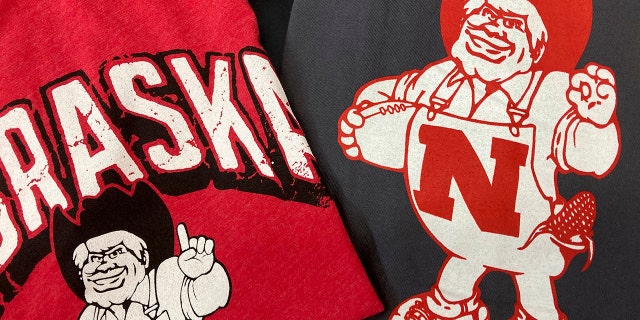 Nebraska Huskers t-shirts featuring new cartoon mascot Herbie Husker, left, and old cartoon mascot, right, are displayed at the Husker Hounds store in Omaha, Neb., Saturday, Jan. 29, 2022. The University of Nebraska-Lincoln has made a change to its cartoon mascot Herbie Husker to eliminate confusion about the meaning of a hand gesture he makes that some people connect with white supremacy.