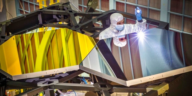 In this Sept. 29, 2014 photo made available by NASA, James Webb Space Telescope Optical Engineer Larkin Carey examines two test mirror segments on a prototype at the Goddard Space Flight Center's giant clean room in Greenbelt, Md.