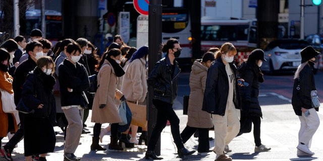 People wearing protective masks to help curb the spread of the coronavirus walk along a pedestrian crossing Friday, Jan. 21, 2022, in Tokyo.  