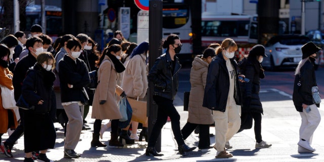 People wearing protective masks to help curb the spread of the coronavirus walk along a pedestrian crossing Friday, Jan. 21, 2022, in Tokyo.