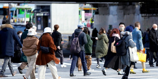 People wearing protective masks to help curb the spread of the coronavirus walk along a pedestrian crossing Friday, Jan. 21, 2022, in Tokyo.