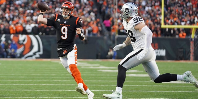 Cincinnati Bengals quarterback Joe Burrow (9) throws while being pressured by Las Vegas Raiders' Maxx Crosby (98) during the first half of an NFL wild-card playoff football game, Saterdag, Jan.. 15, 2022, in Cincinnati.