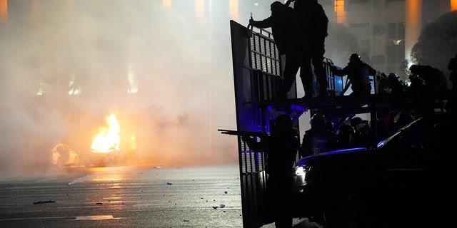 A police car on fire as riot police prepare to stop protesters in the center of Almaty, Kazakhstan, Wednesday, Jan. 5, 2022.