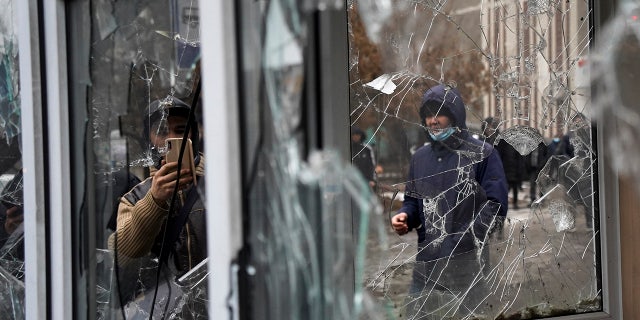 A man takes a photo of windows of a police kiosk damaged by demonstrators during a protest in Almaty, Kazakhstan, Wednesday, Jan. 5, 2022. (AP Photo/Vladimir Tretyakov)