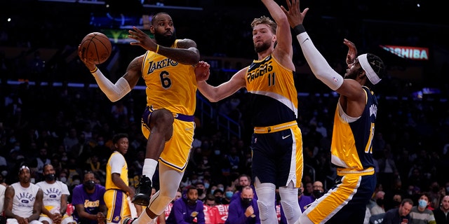 Penyerang Los Angeles Lakers LeBron James (6) melewati pemain depan Indiana Pacers Domantas Sabonis (11) dan pemain depan O'Shea Brissett (12) pada paruh pertama pertandingan bola basket NBA di Los Angeles, Rabu, 19 Januari 2022.