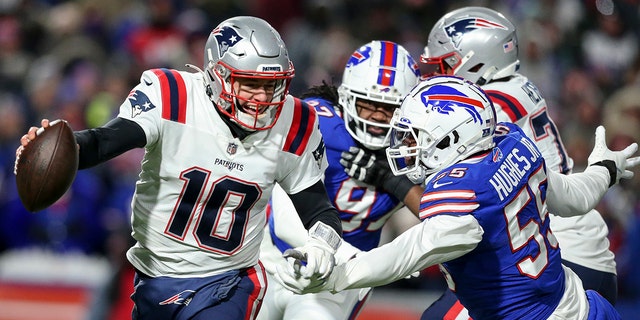 New England Patriots quarterback Mac Jones (10) runs the ball under pressure from Buffalo Bills defensive end Jerry Hughes (55) during the first half of an NFL wild-card playoff football game, Saturday, Jan. 15, 2022, in Orchard Park, N.Y.