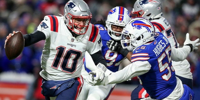 New England Patriots quarterback Mac Jones (10) runs the ball under pressure from Buffalo Bills defensive end Jerry Hughes (55) during the first half of an NFL wild-card playoff football game, Saturday, Jan. 15, 2022, in Orchard Park, N.Y.