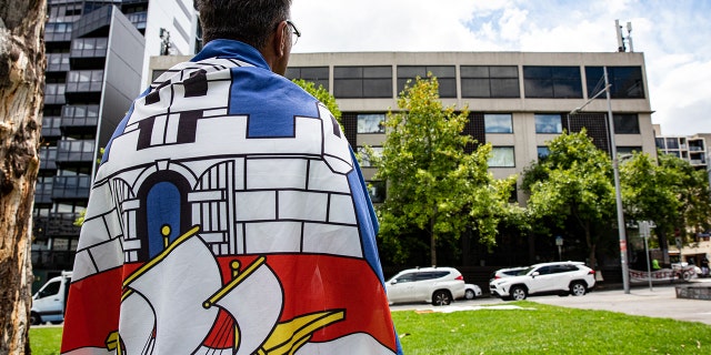 A supporter of Novak Djokovic wears a Serbian flag as he waits outside Park Hotel where Djokovic was taken pending his removal from the country after his visa was canceled by the Australian Border Force on January 06, 2022 in Melbourne, 澳大利亚.