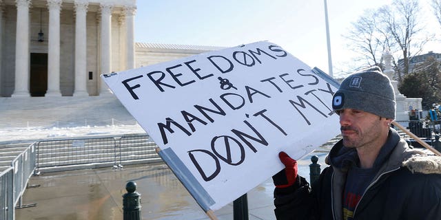 A lone protester stands outside the U.S. Supreme Court as it hears arguments against the Biden administration's nationwide vaccine-or-testing COVID-19 mandates, in Washington, Jan. 7, 2022.