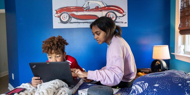 Fulton County Public Schools 8th grader, Ceani Williams, helps her 5th grade brother, Kareem Williams, with his classwork during a virtual learning day at their residence in Milton, Georgia.