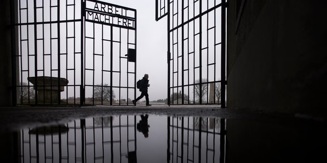 A man walks behind a gate of the Sachsenhausen Nazi death camp that reads 'Arbeit macht Frei' (Work sets you free) in Oranenburg, 30 kilometers (18 miles) north of Berlin, Germany, Tuesday, Jan. 25, 2022. 