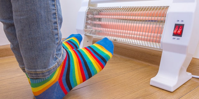 A person wearing bright rainbow-colored socks and warming cold feet near an electric heater. Infrared halogen heaters at home.