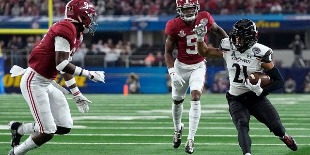 Cincinnati wye ontvanger Tyler Scott (21) runs for gain after catching a pass as Alabama's Jalyn Armour-Davis (5) and Jordan Battle (9) defend during the first half of the Cotton Bowl NCAA College Football Playoff semifinal game, Vrydag, Des. 31, 2021, in Arlington, Texas.