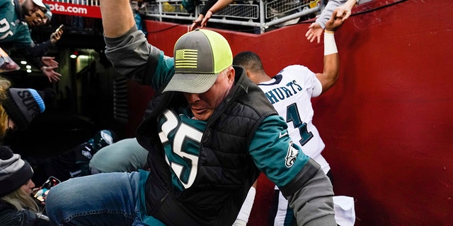 Fans fall onto Philadelphia Eagles quarterback Jalen Hurts (1) after the railing collapsed at the end of a game Jan. 2, 2022, in Landover, Md.