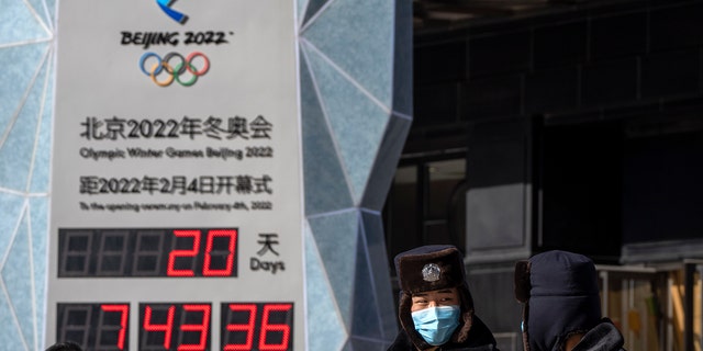 Police officers wearing face masks to protect against COVID-19 walk past a clock counting down the time until the opening ceremony of the 2022 Olimpiadi invernali di Pechino, Sabato, Jan. 15, 2022.