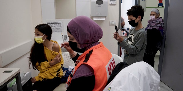 N'amah Yetzhak Abohaikal, a volunteer with the women's unit of United Hatzalah emergency service, prepares administer the COVID-19 vaccine to a teen girl as her brother and grandmother watch, at Clalit Health Services in Mevaseret Zion, Tuesday, Jan. 11, 2022.