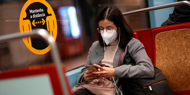 A young woman wearing a face mask looks at her phone on a subway train in Lisbon, Jan. 6, 2022. 