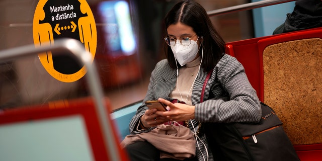A young woman wearing a face mask looks at her phone on a subway train in Lisbon, Jan. 6, 2022.