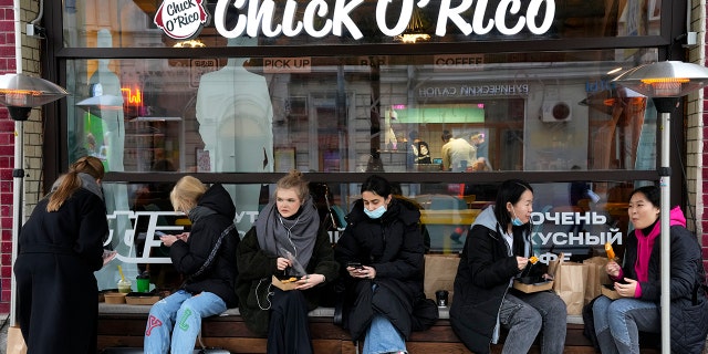 People eat their takeaway food sitting outside a cafe that is d due to coronavirus in Moscow, Russia, Friday, Oct. 29, 2021.