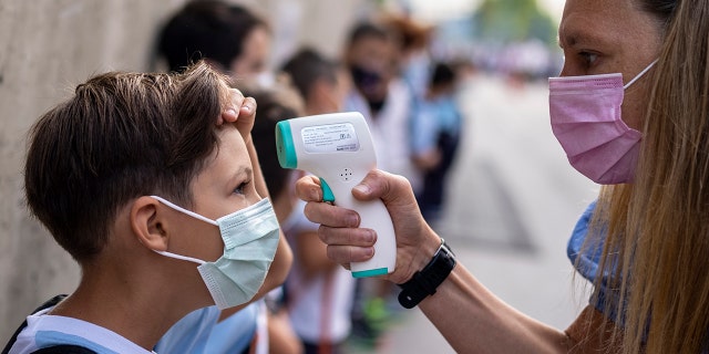 A teacher wearing a face mask to protect against the spread of coronavirus checks the temperature of her student at Maestro Padilla school as the new school year begins in Madrid, Sept. 7, 2021.