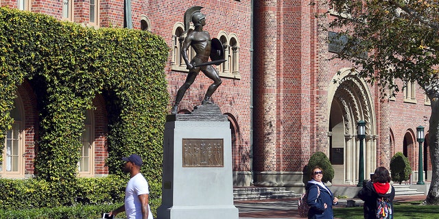 In this March 12, 2019, file photo, people pose for photos in front of the iconic Tommy Trojan statue on the campus of the University of Southern California in Los Angeles. 