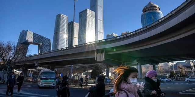 Commuters wearing face masks to help protect against the coronavirus walk across an intersection in the central business district in Beijing, Thursday, Jan. 13, 2022. 