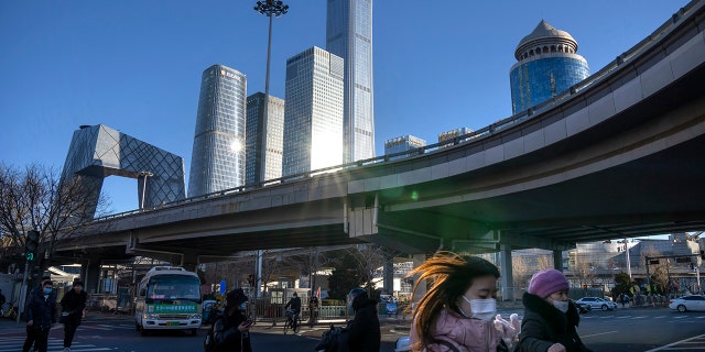 Commuters wearing face masks to help protect against the coronavirus walk across an intersection in the central business district in Beijing, Thursday, Jan. 13, 2022.