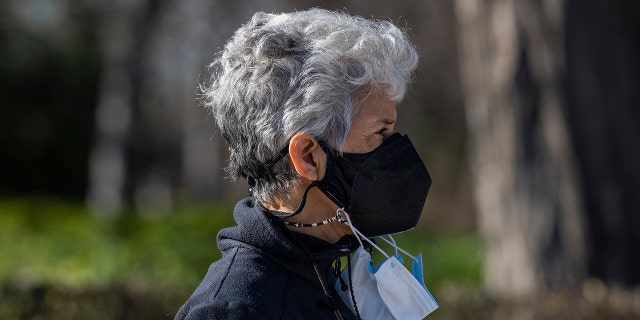A woman wearing multiple face masks walks in the Retiro park in Madrid, Spain, Wednesday, Jan. 12, 2022.