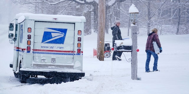 Un transportista del Servicio Postal de EE. UU. entrega un paquete durante una tormenta de nieve el viernes 7 de enero de 2022 en East Derry, New Hampshire.  Se espera que una tormenta de invierno deje caer alrededor de medio pie de nieve en el área.